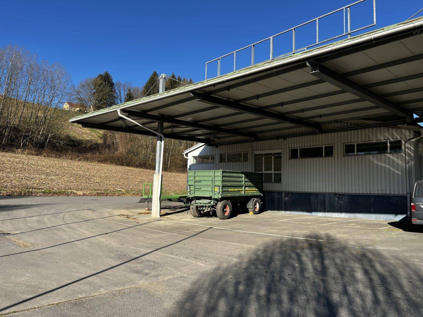 Überdachter Parkbereich oder Carport mit einem Anhänger darunter, unter strahlend blauem Himmel.