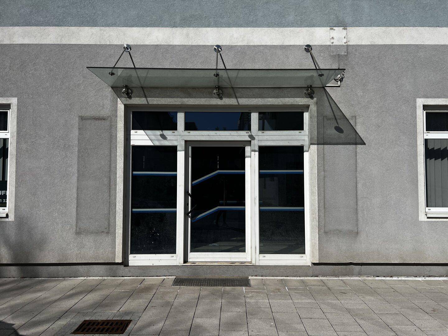 Gebäudeeingang mit einer modernen Glasüberdachung und großen Fenstertüren.