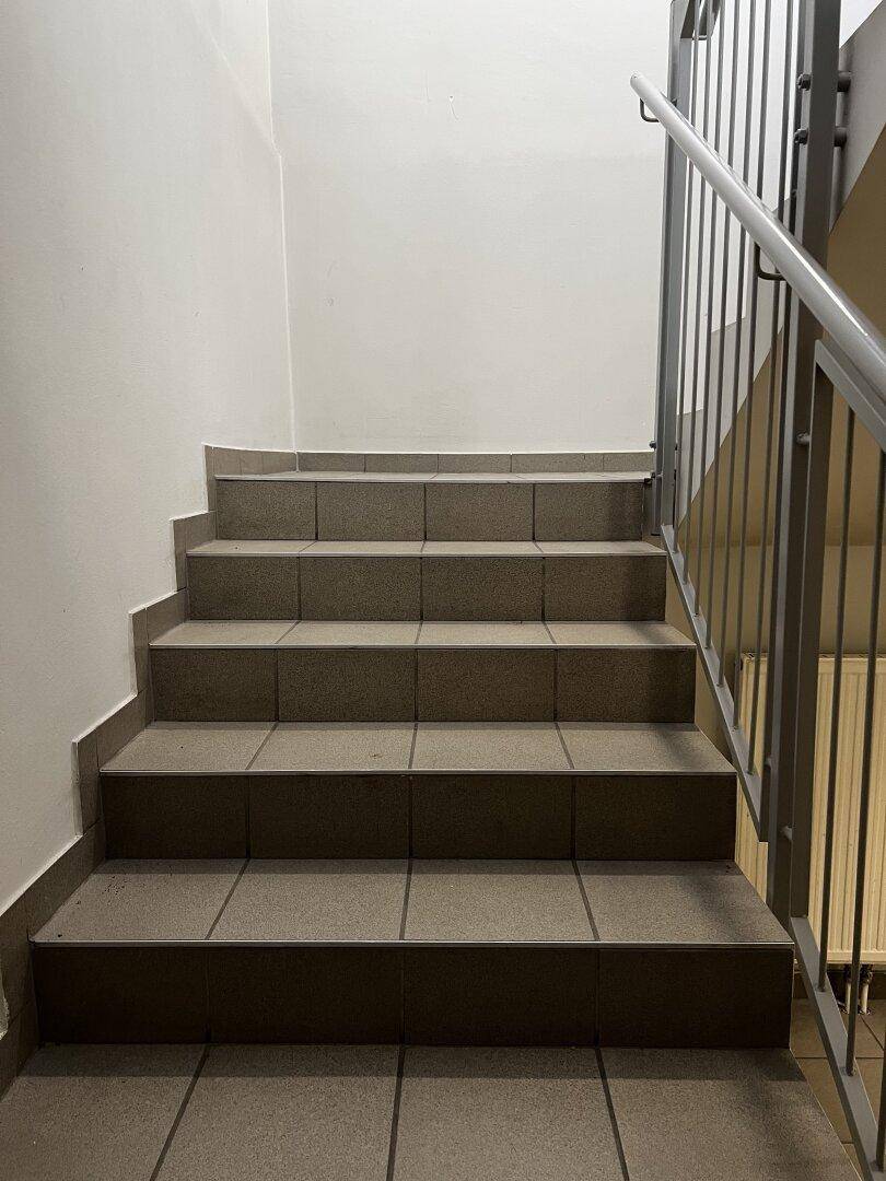 Treppenhaus mit Fliesenstufen und einem Metallgeländer, das in die obere Etage führt.