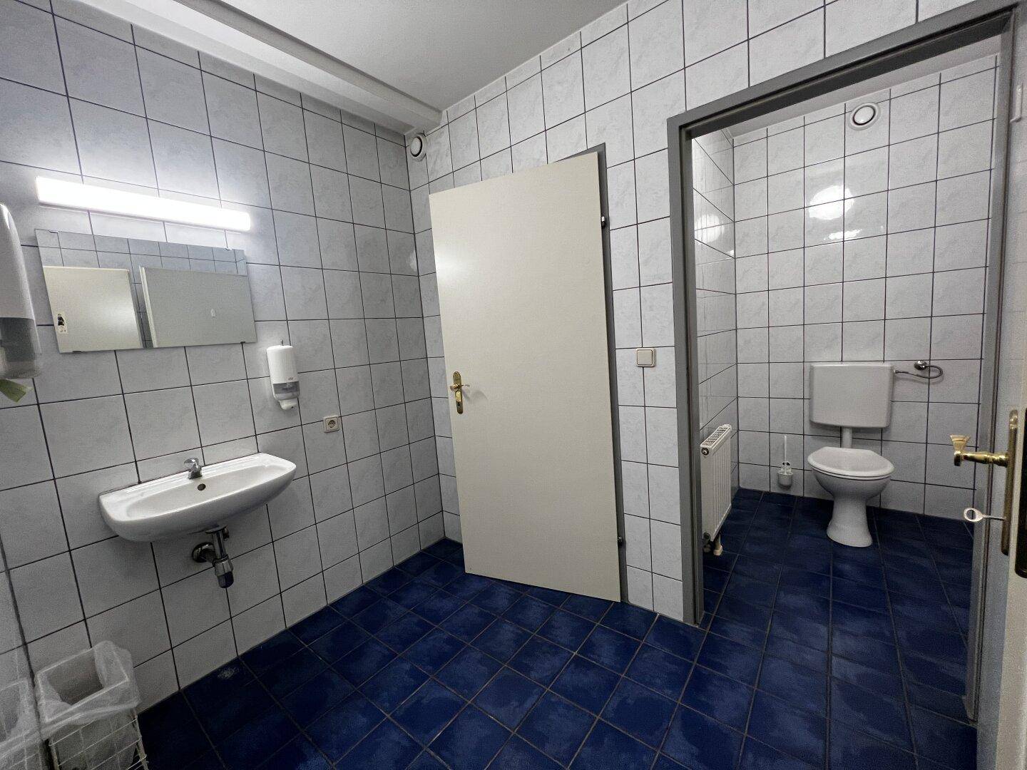 Einfaches Badezimmer mit blauen und weißen Fliesen, Waschbecken und Toilette.