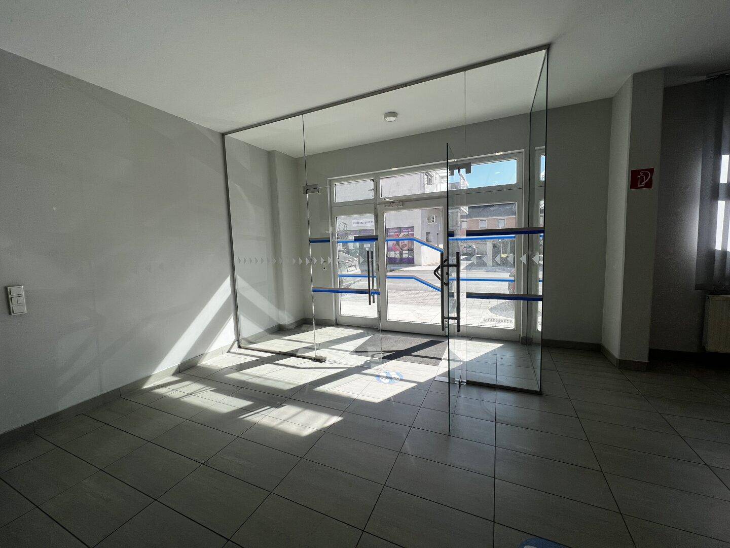 Geräumiger Eingangsbereich mit Fliesenboden und großen Glasfenstern, die viel Tageslicht hereinlassen.