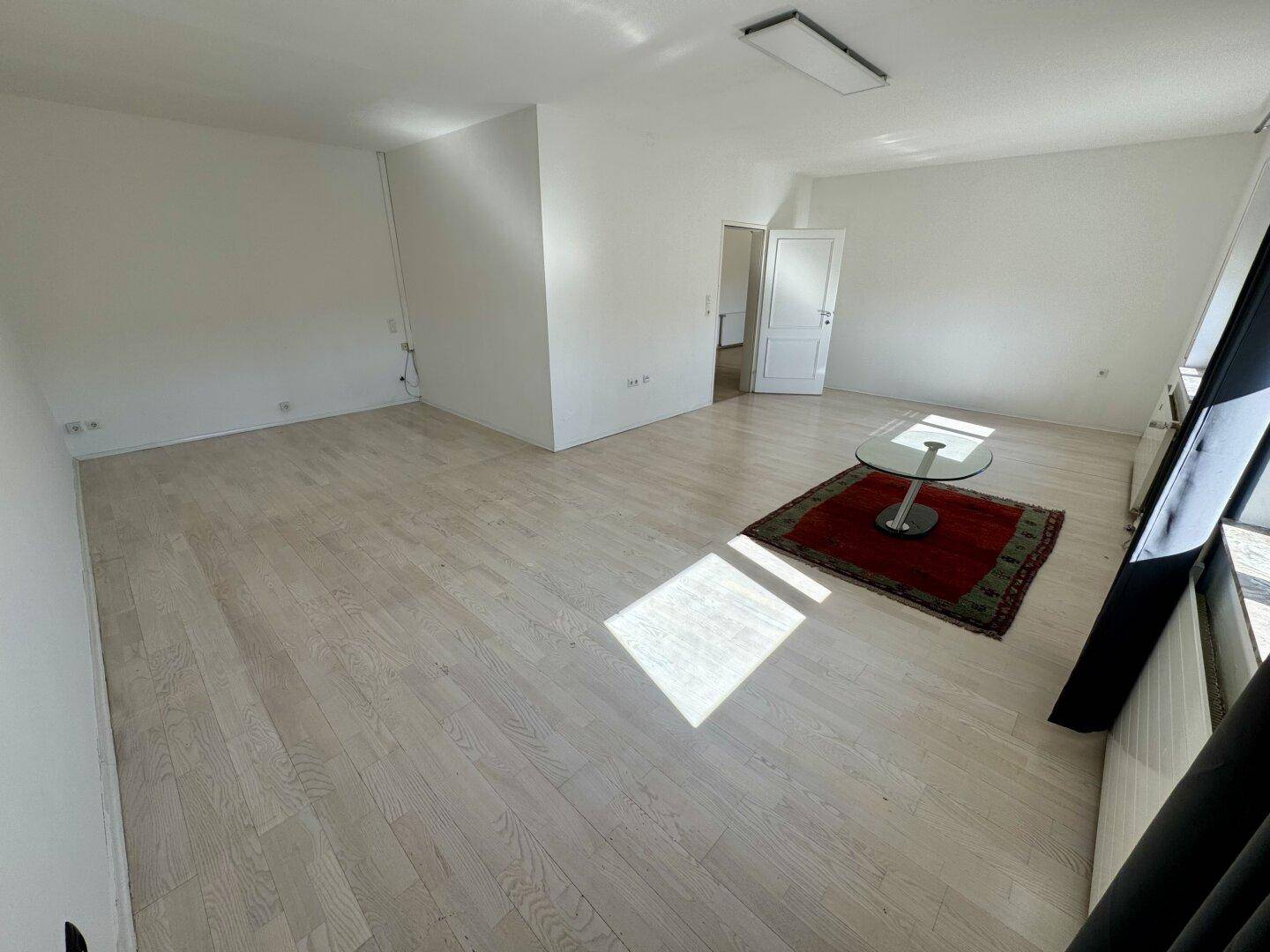 Großes, helles Wohnzimmer mit Holzboden und viel Sonnenlicht, das den Raum durchflutet.
