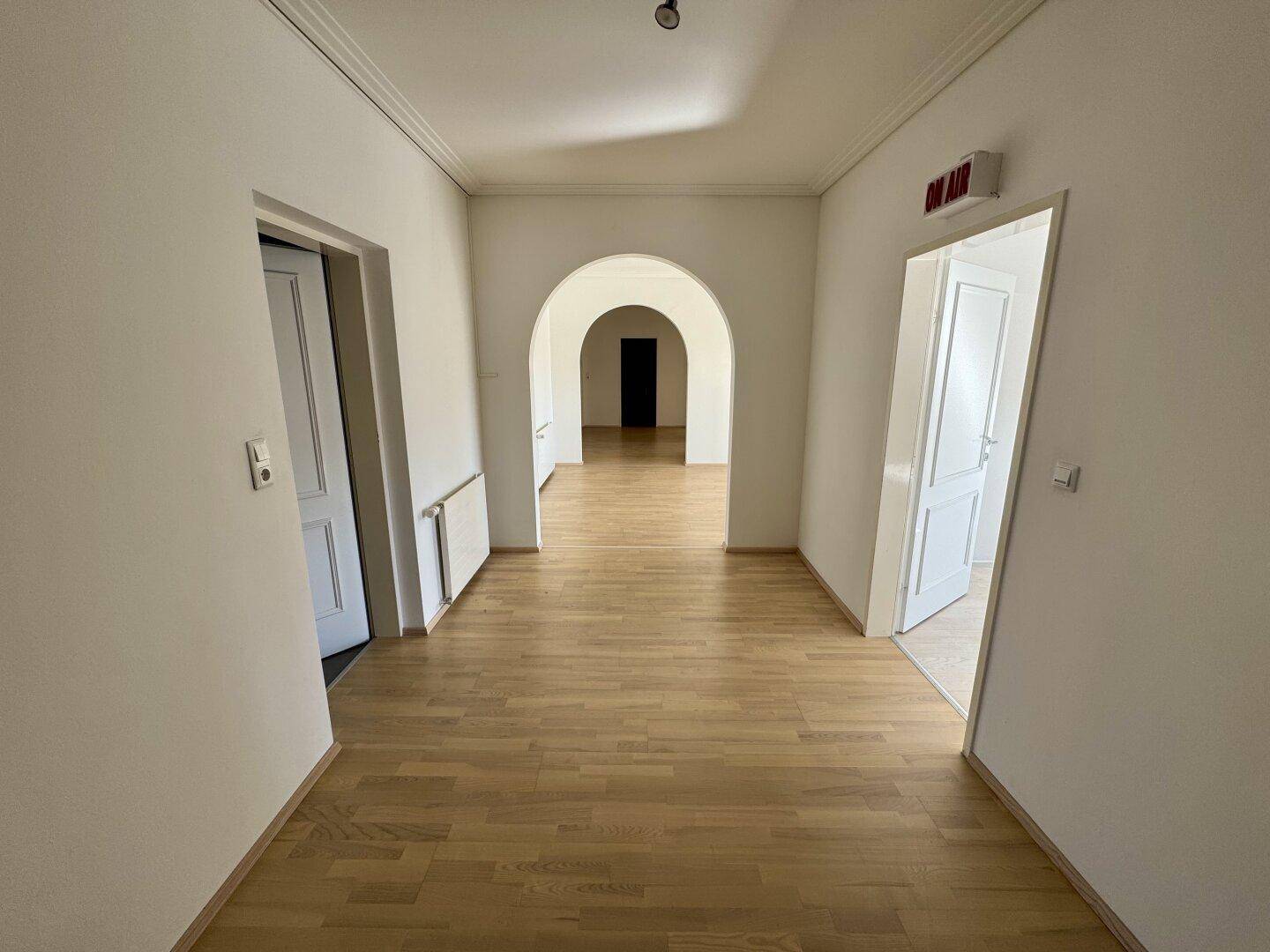 Langer Flur mit hellem Parkettboden und mehreren Türen, der zu weiteren Räumen führt.