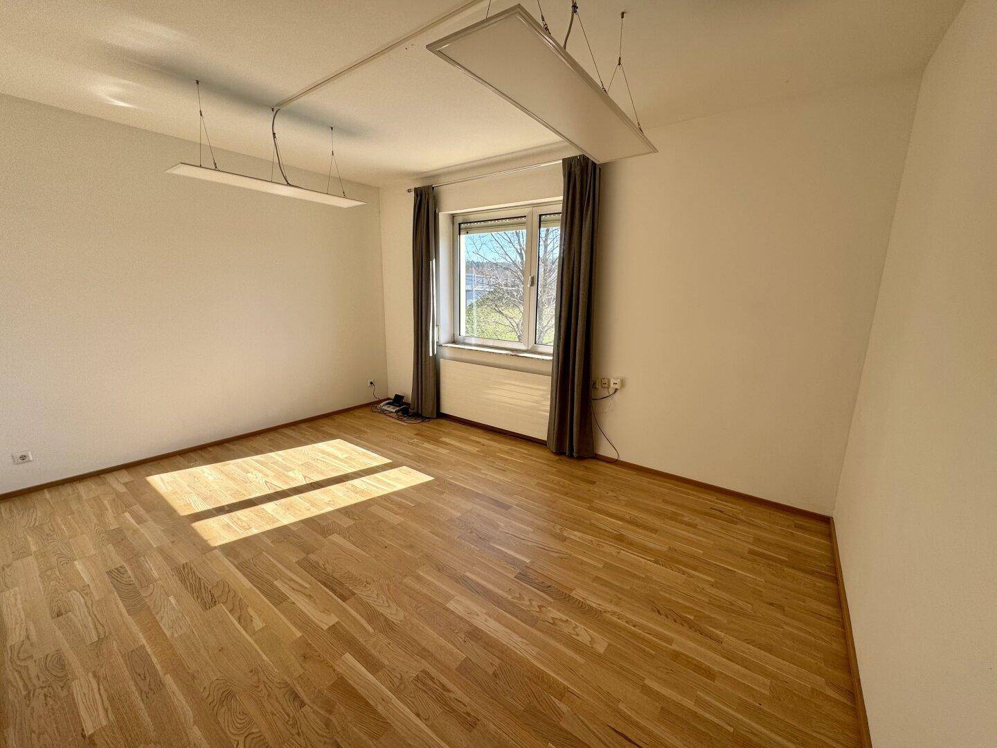 Geräumiges Schlafzimmer mit Holzboden und großem Fenster, das den Raum hell erscheinen lässt.