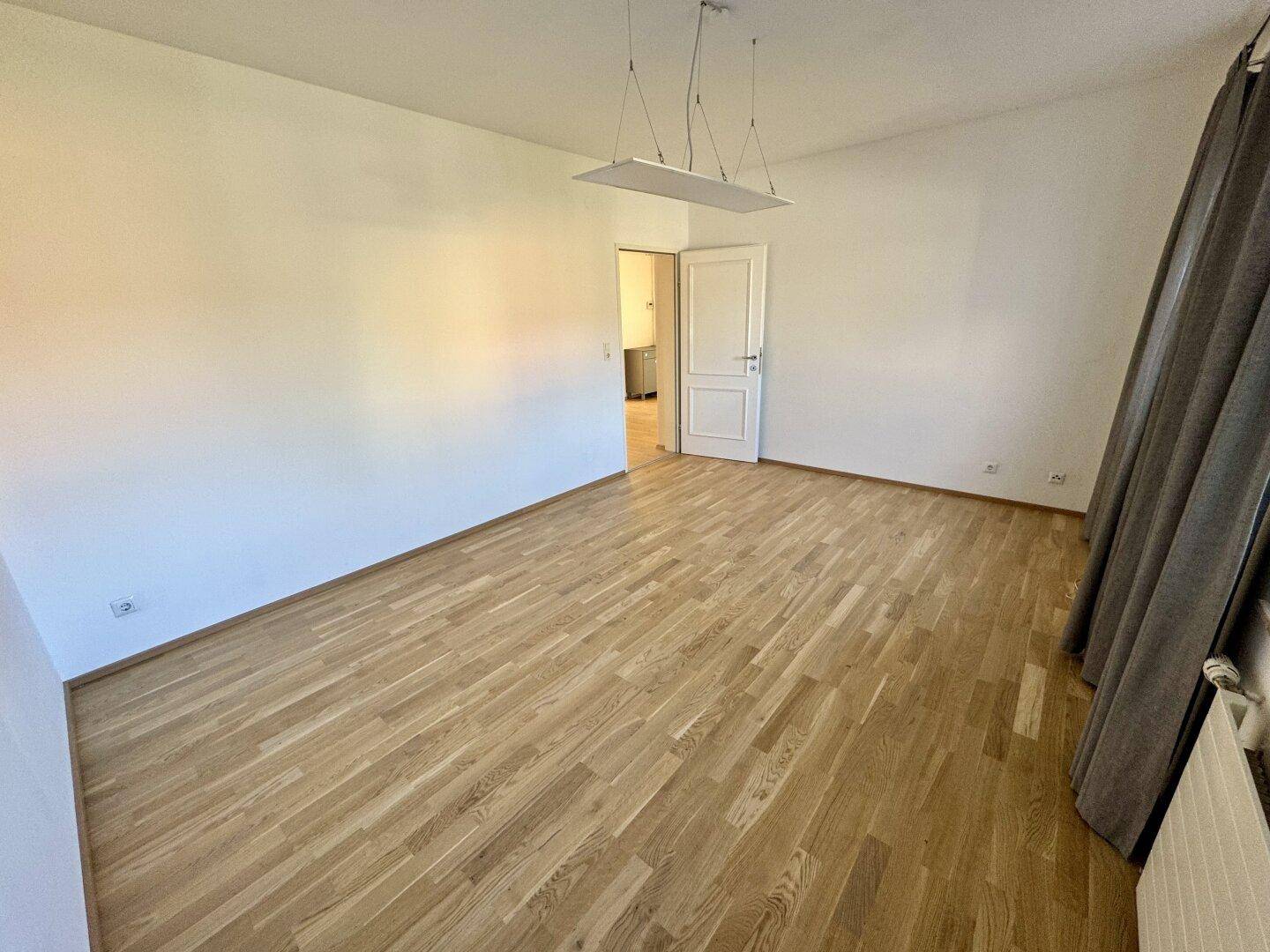 Helles Zimmer mit Parkettboden und Vorhängen, das viel natürliches Licht empfängt.