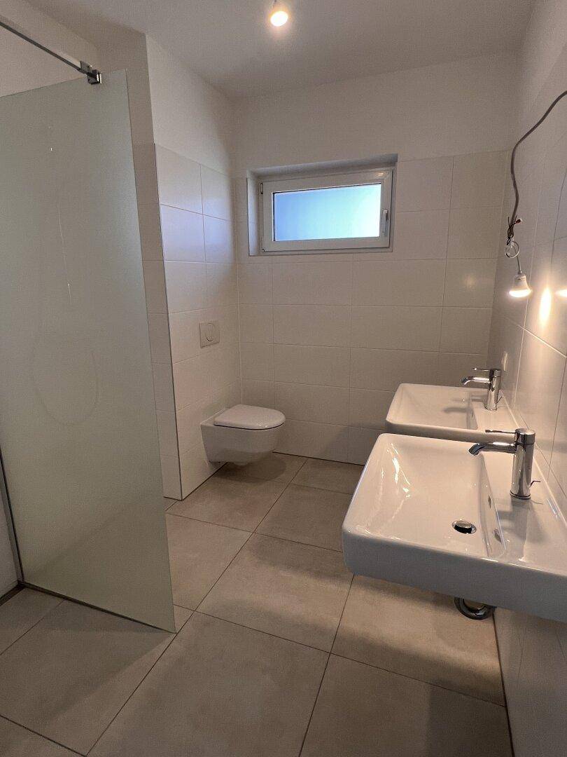 Modernes Badezimmer mit Doppelwaschbecken, bodengleicher Dusche und Fenster für Tageslicht.