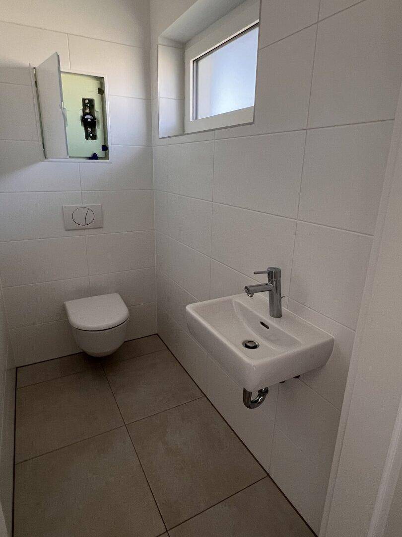 Gäste-WC mit modernem Wand-WC, kleinem Waschbecken und Fenster für Belüftung.