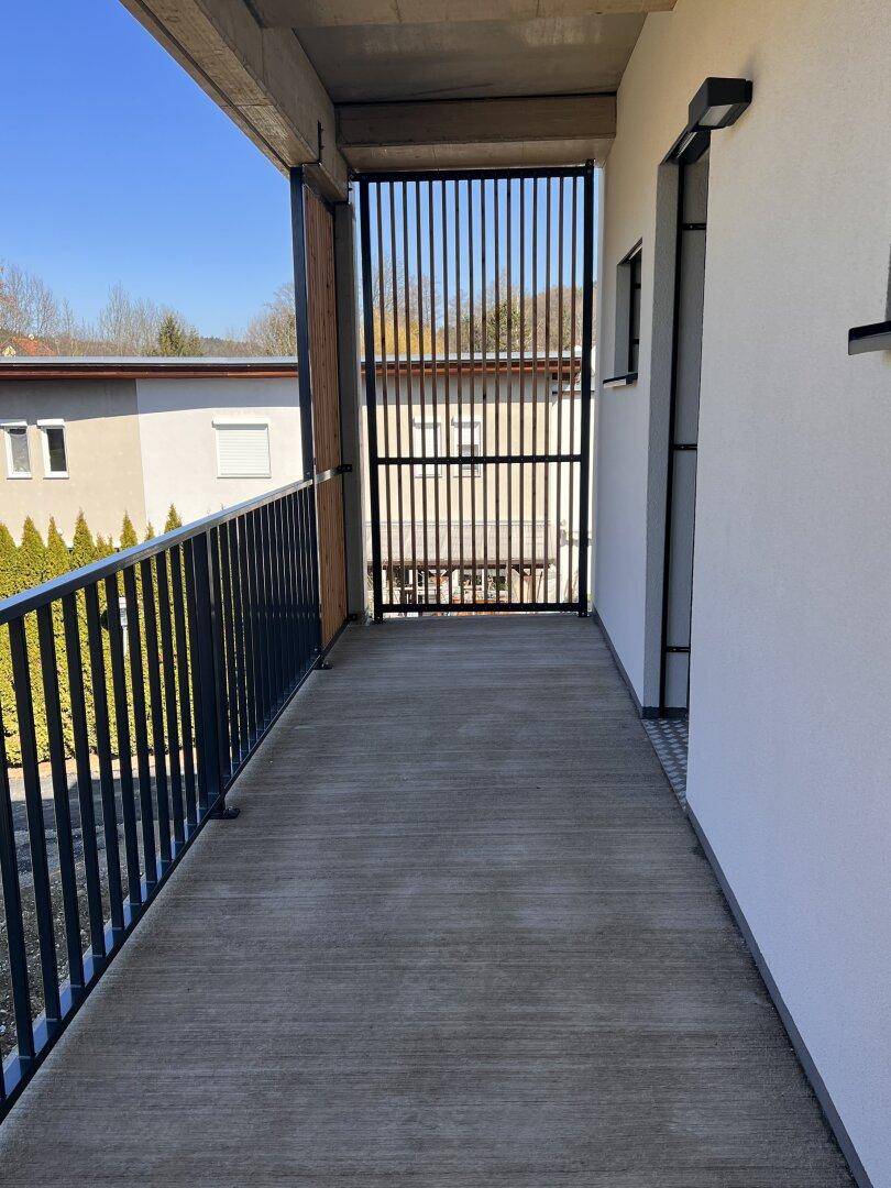 Schmaler Balkon mit Betonboden und schwarzem Metallgeländer, bietet Zugang zum Außenbereich.