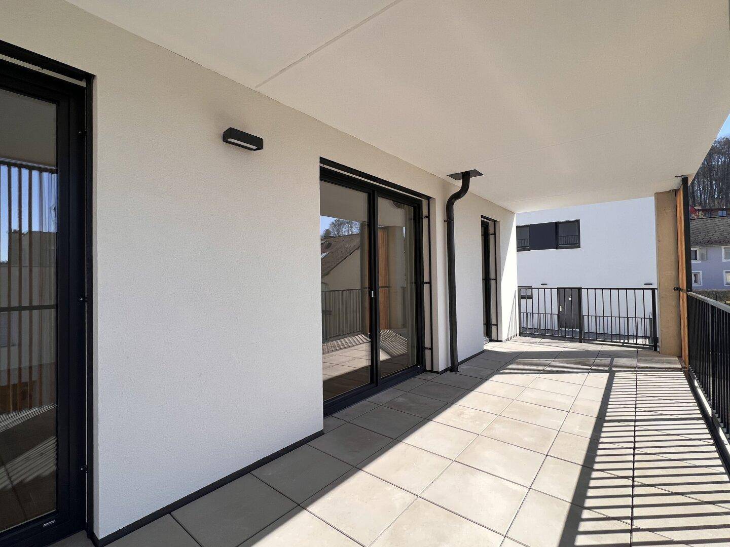 Geräumiger, sonniger Balkon mit modernen Fliesen und schwarzem Geländer, ideal für entspannte Stunden im Freien.