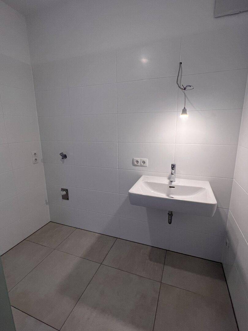 Helles Badezimmer mit weißen Fliesen und einem modernen Einzelwaschbecken, bereit für die Einrichtung.