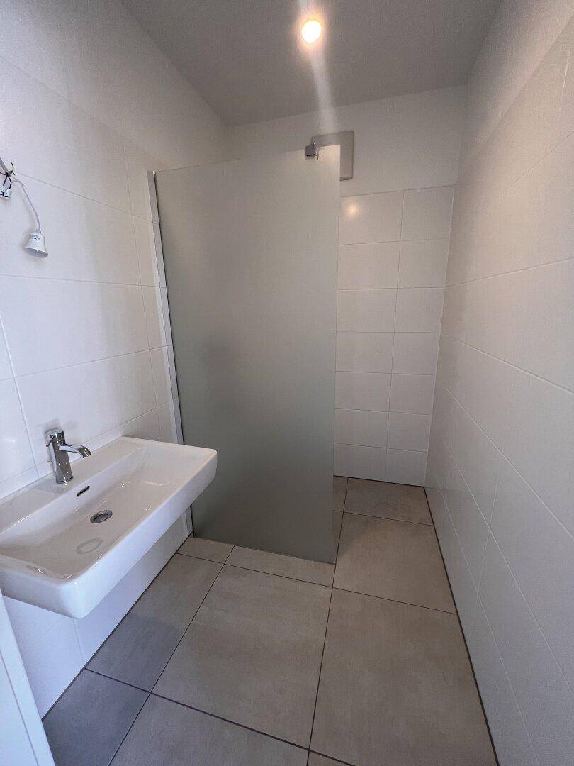Modernes Badezimmer mit weißem Waschbecken, Duschbereich und hellen Fliesen.