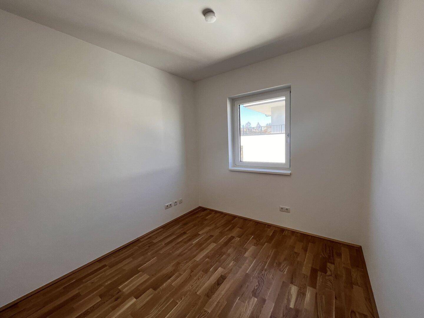 Kleines, helles Zimmer mit Holzboden und einem Fenster, geeignet als Kinderzimmer oder Büro.