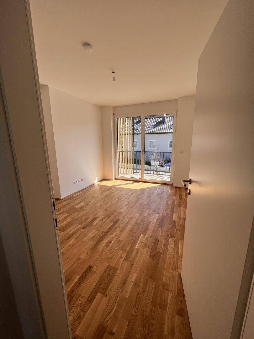 Schlafzimmer mit Holzboden und Zugang zu einem Balkon, bietet viel natürliches Licht.