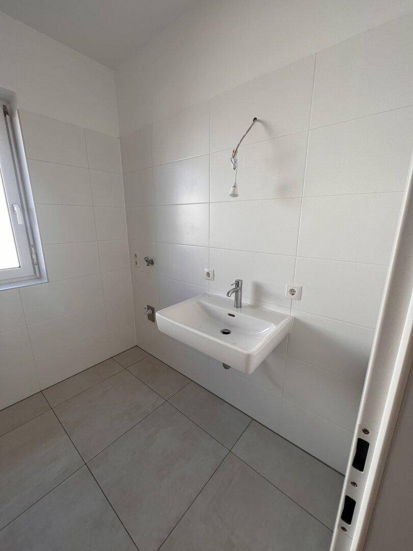 Helles Badezimmer mit Waschbecken und Fenster, ausgestattet mit modernen Fliesen.