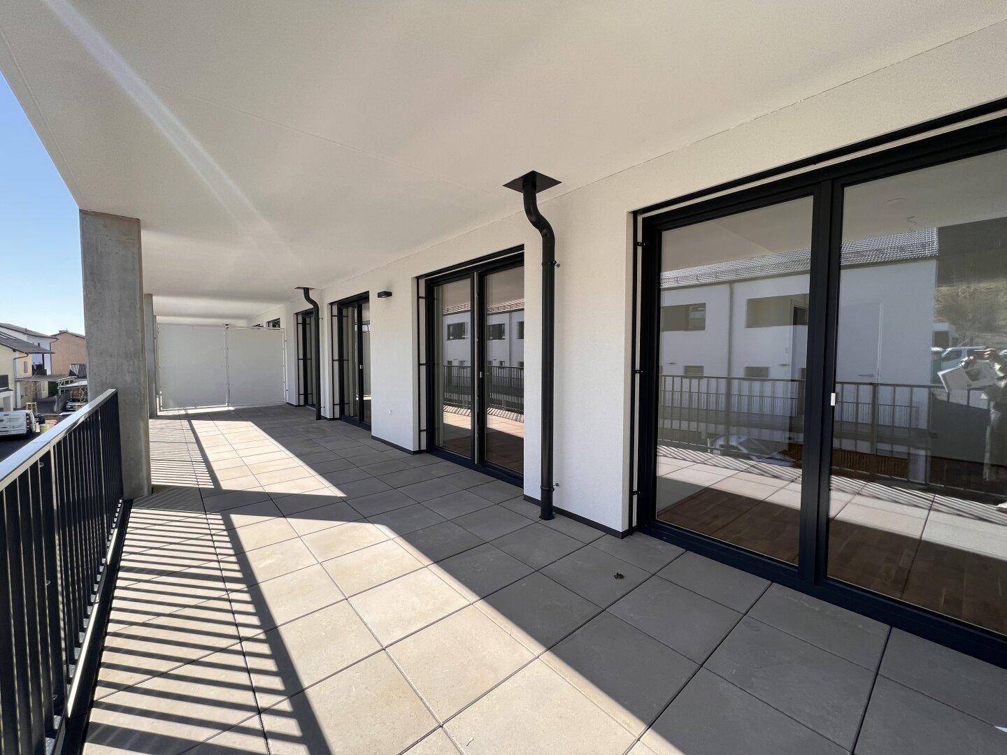 Langer Balkon mit Fliesenboden und großen Glasfronten, ideal für sonnige Stunden.