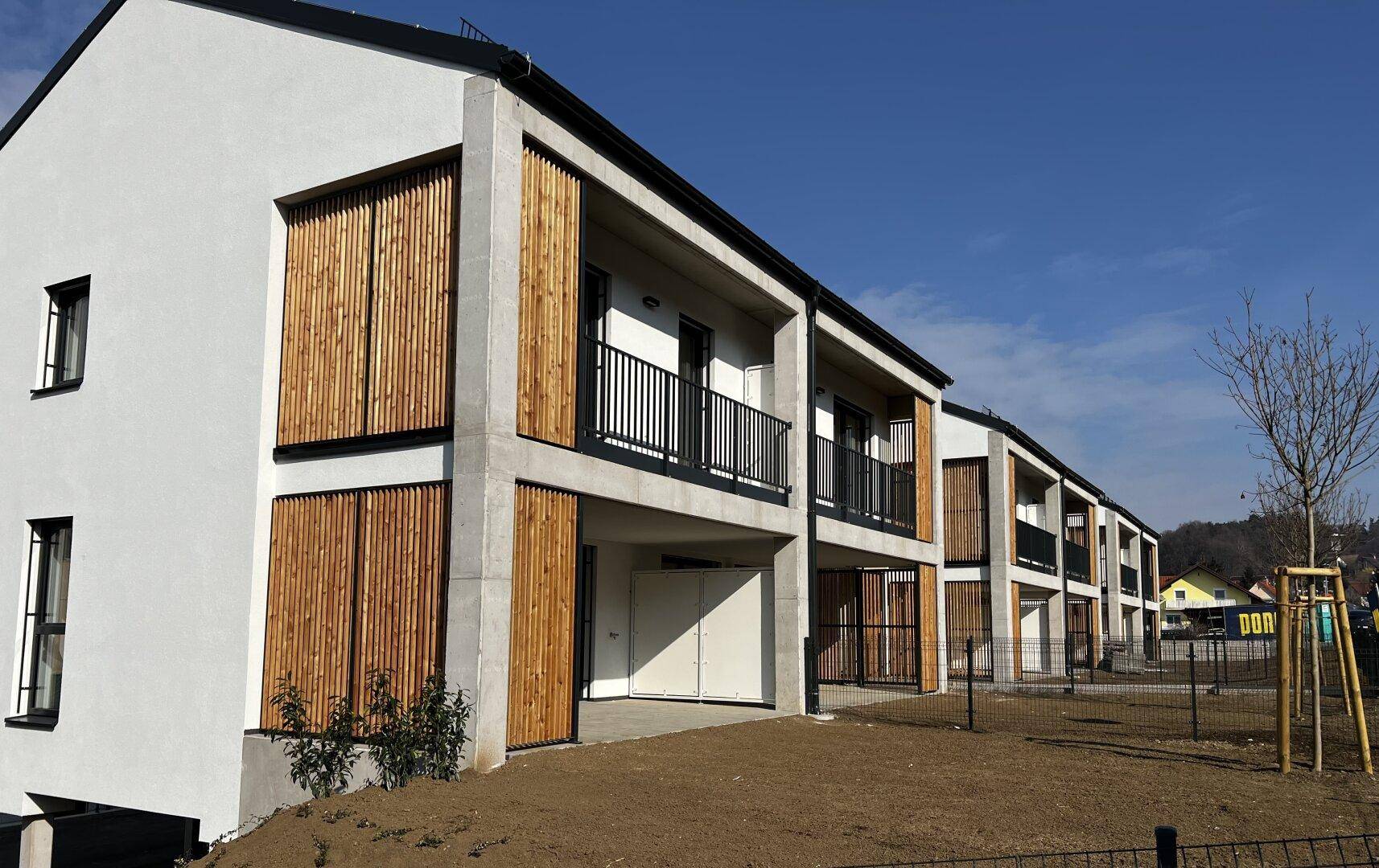 Seitenansicht eines modernen Reihenhauses mit Holzlamellen und Balkonen in sonniger Lage.