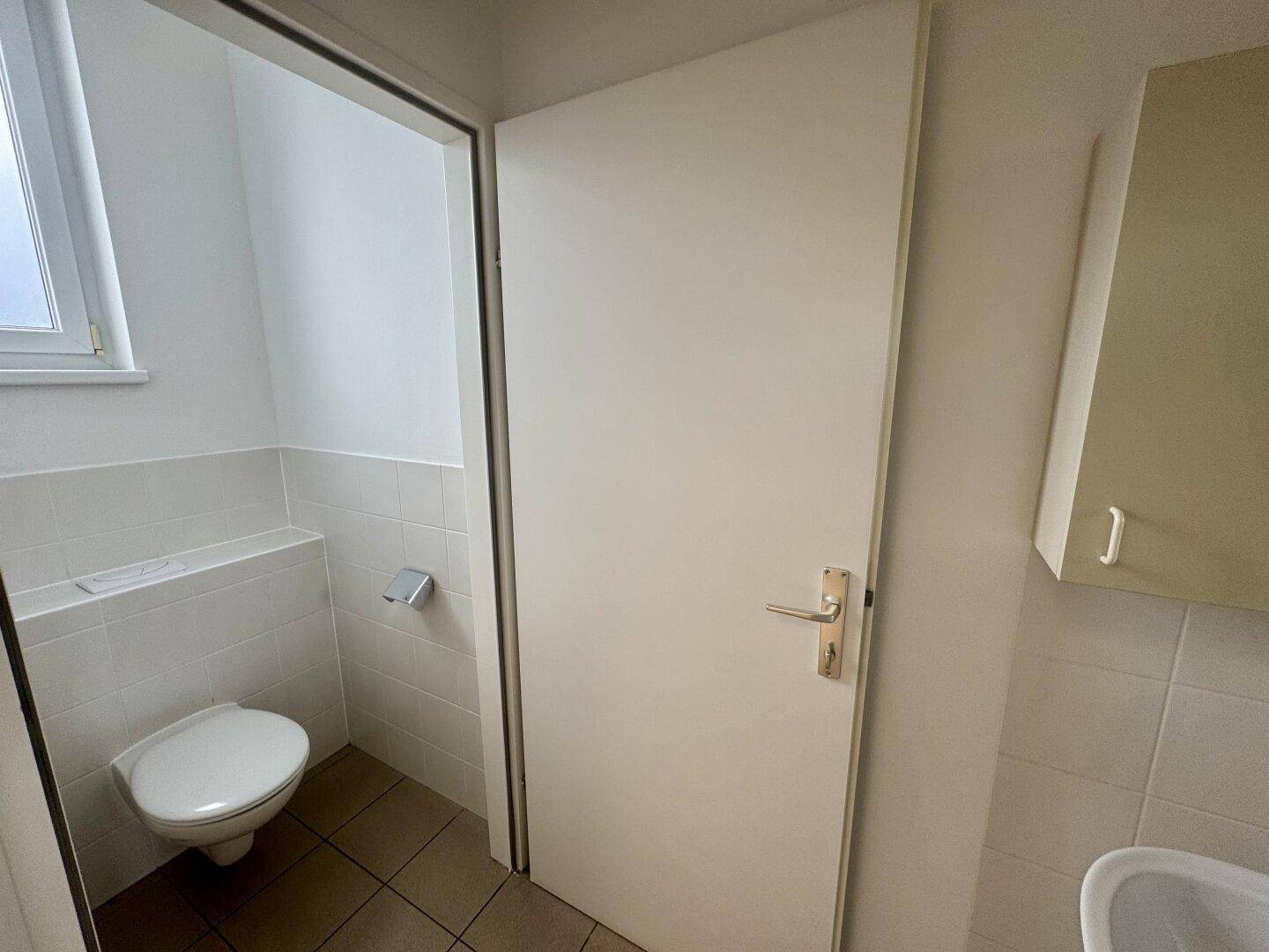 Helle Gästetoilette mit Fenster, Wand-WC und Fliesenboden, in einem gepflegten Zustand.