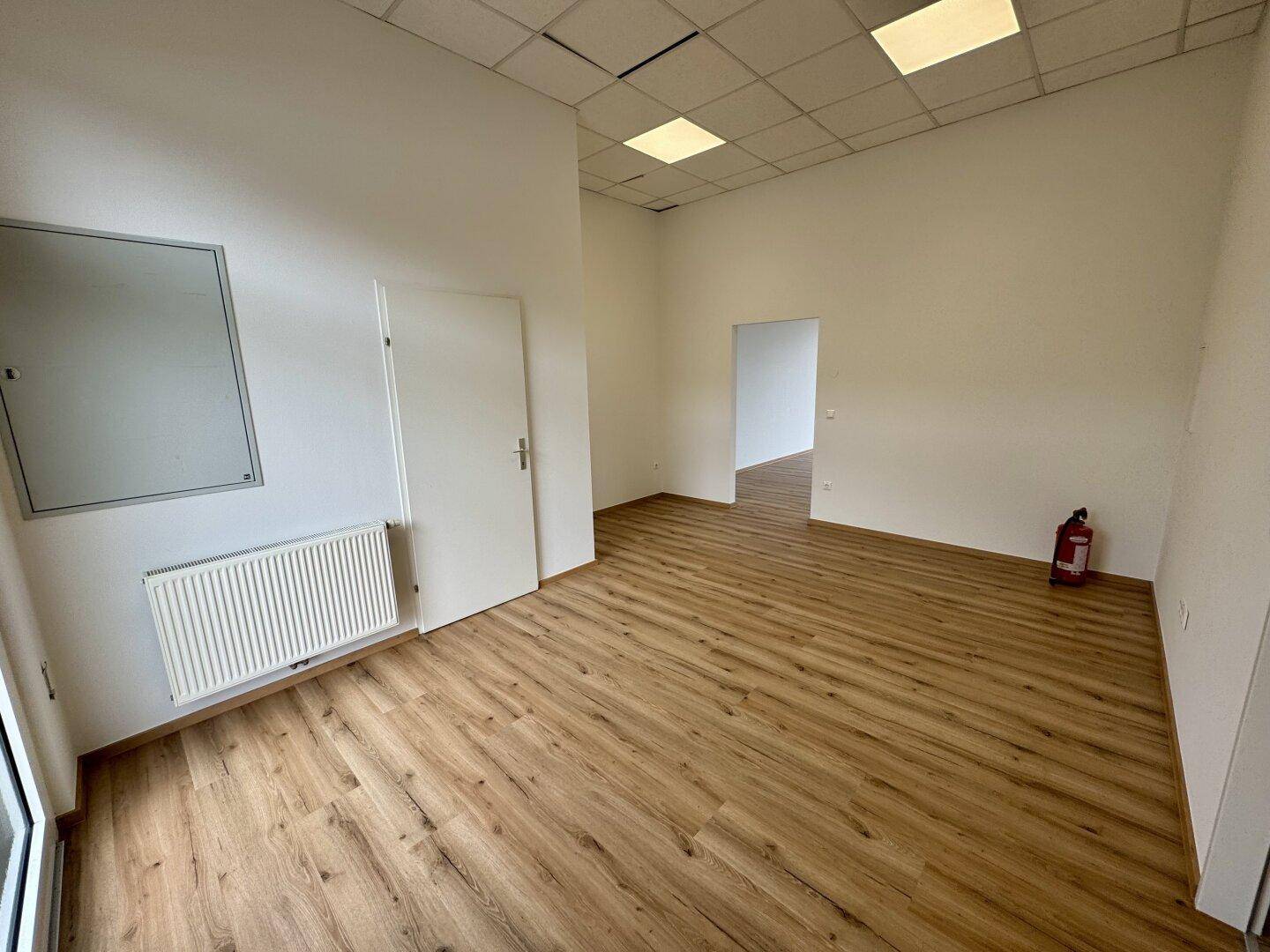 Gewerberaum mit Laminatboden, Heizkörper und Zugang zu weiteren Räumen, bereit zur Nutzung.