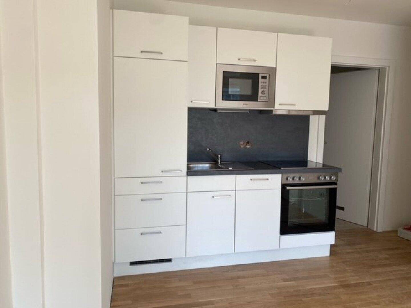 Moderne Einbauküche mit weißen Schränken, integrierter Mikrowelle und Backofen.