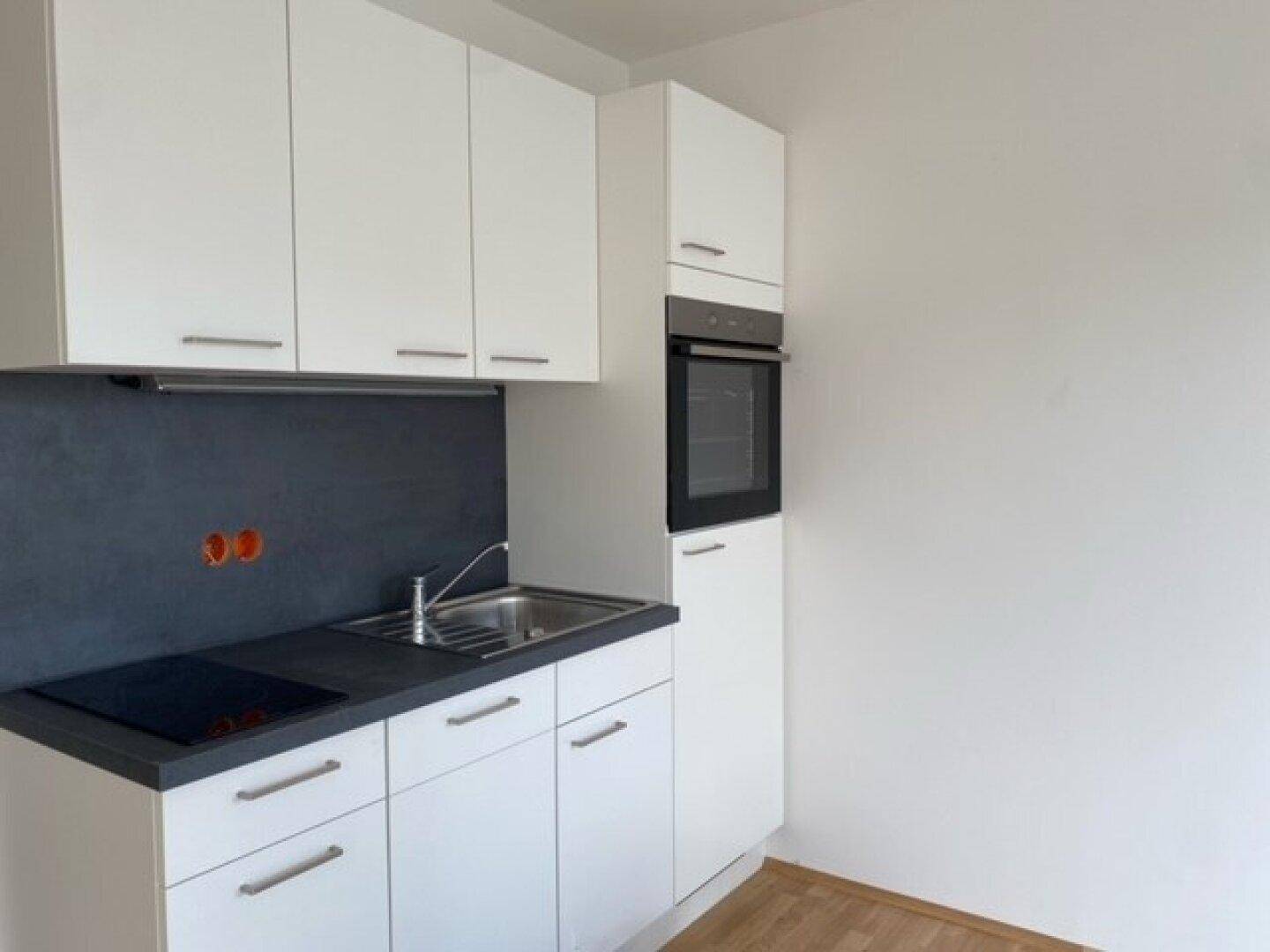 Kompakte weiße Küche mit dunkler Arbeitsplatte, integriertem Kochfeld und Backofen.