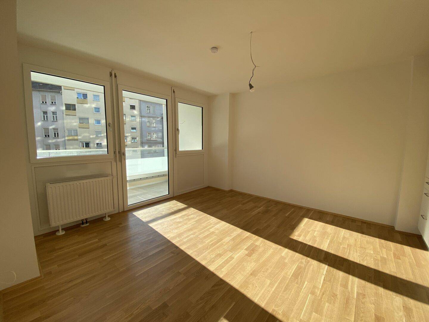 Helles Wohnzimmer mit Parkettboden, großen Fenstern und Zugang zum Balkon.