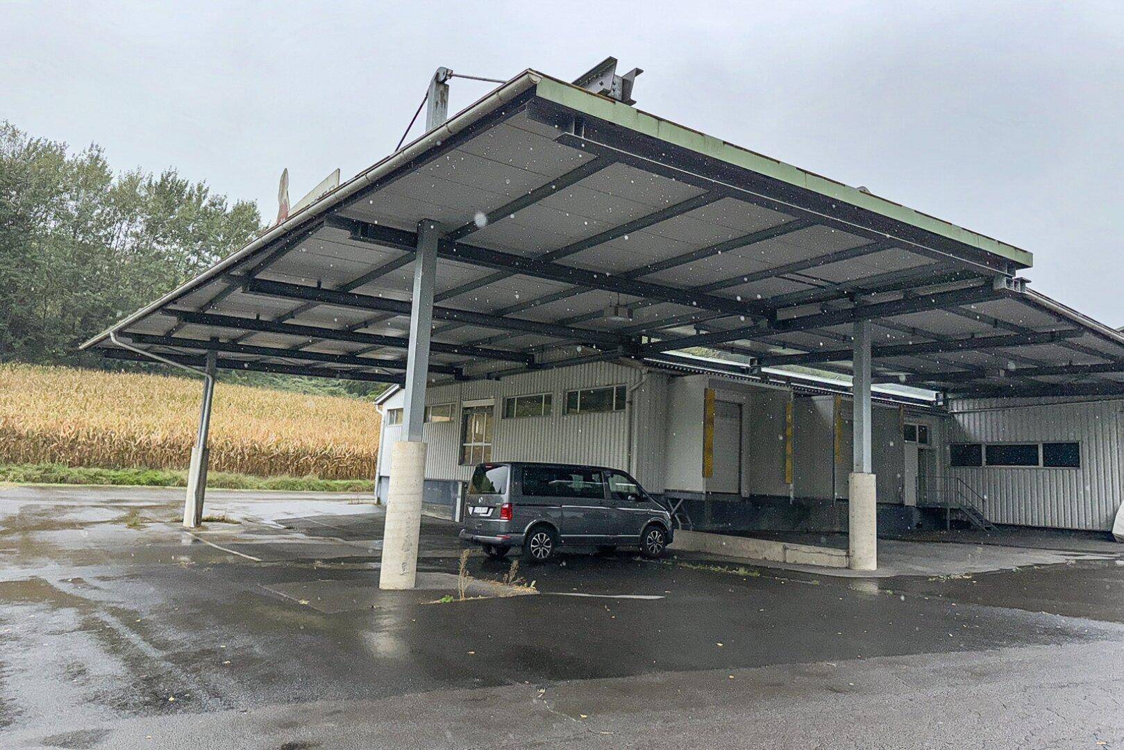 Gewerbegebäude mit weitläufigem Vordach und Parkmöglichkeiten, umgeben von ländlicher Landschaft bei leichtem Schneefall.