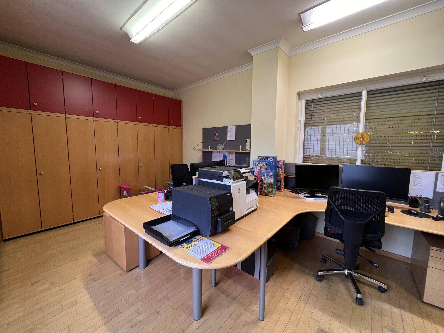 Geräumiges Büro mit großem Schreibtisch, Computern und eingebauten Schränken an der Wand.