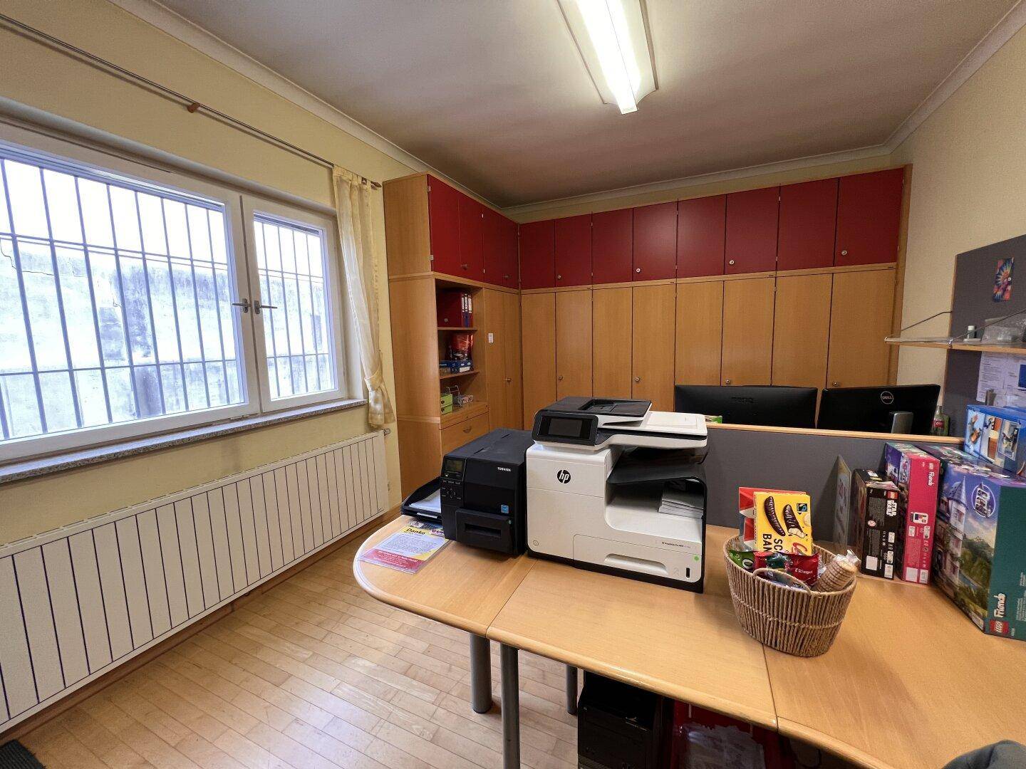 Büroansicht mit Fenster, Heizkörper und Holzschränken, die viel Stauraum bieten.