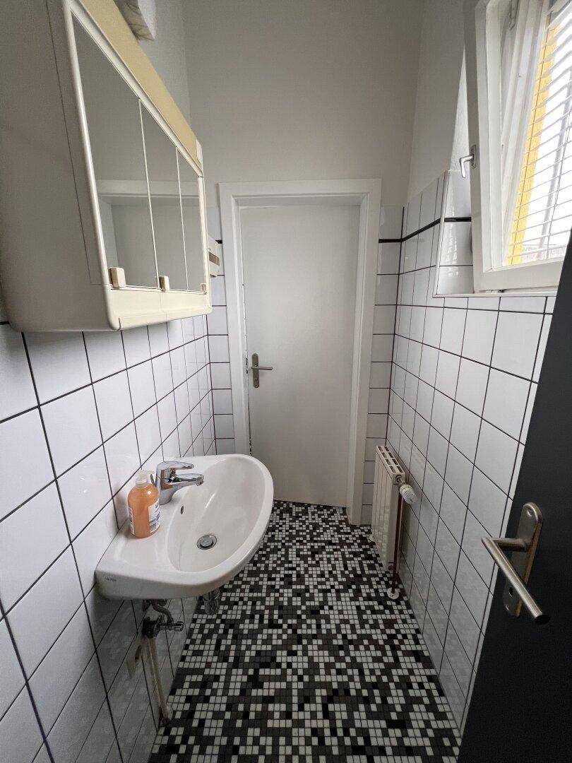 Kleines Badezimmer mit Waschbecken, Spiegelschrank und schwarz-weiß gefliestem Boden.
