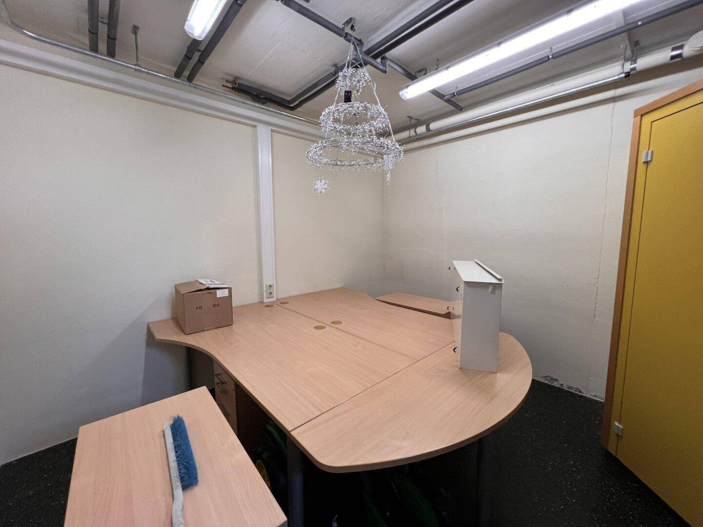 Büro oder Arbeitsbereich im Untergeschoss mit großem Schreibtisch und sichtbaren Deckeninstallationen.