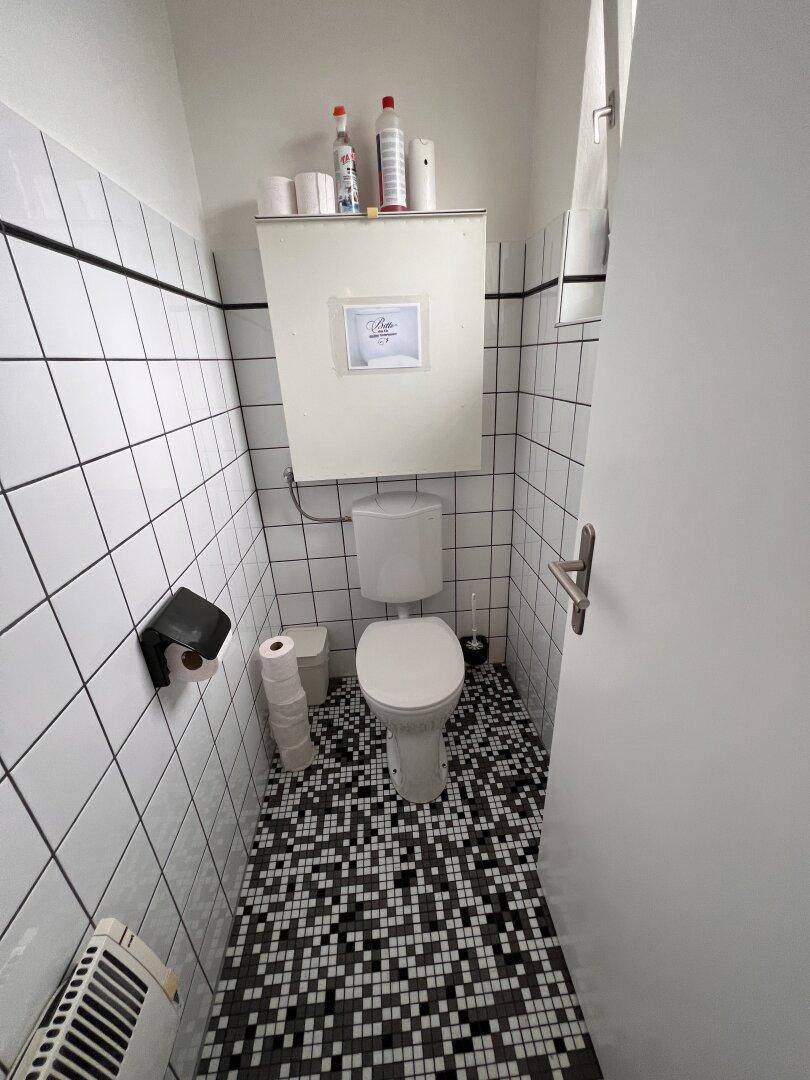 Separate Toilette mit WC, weiß gefliesten Wänden und einem markanten schwarz-weiß gemusterten Boden.