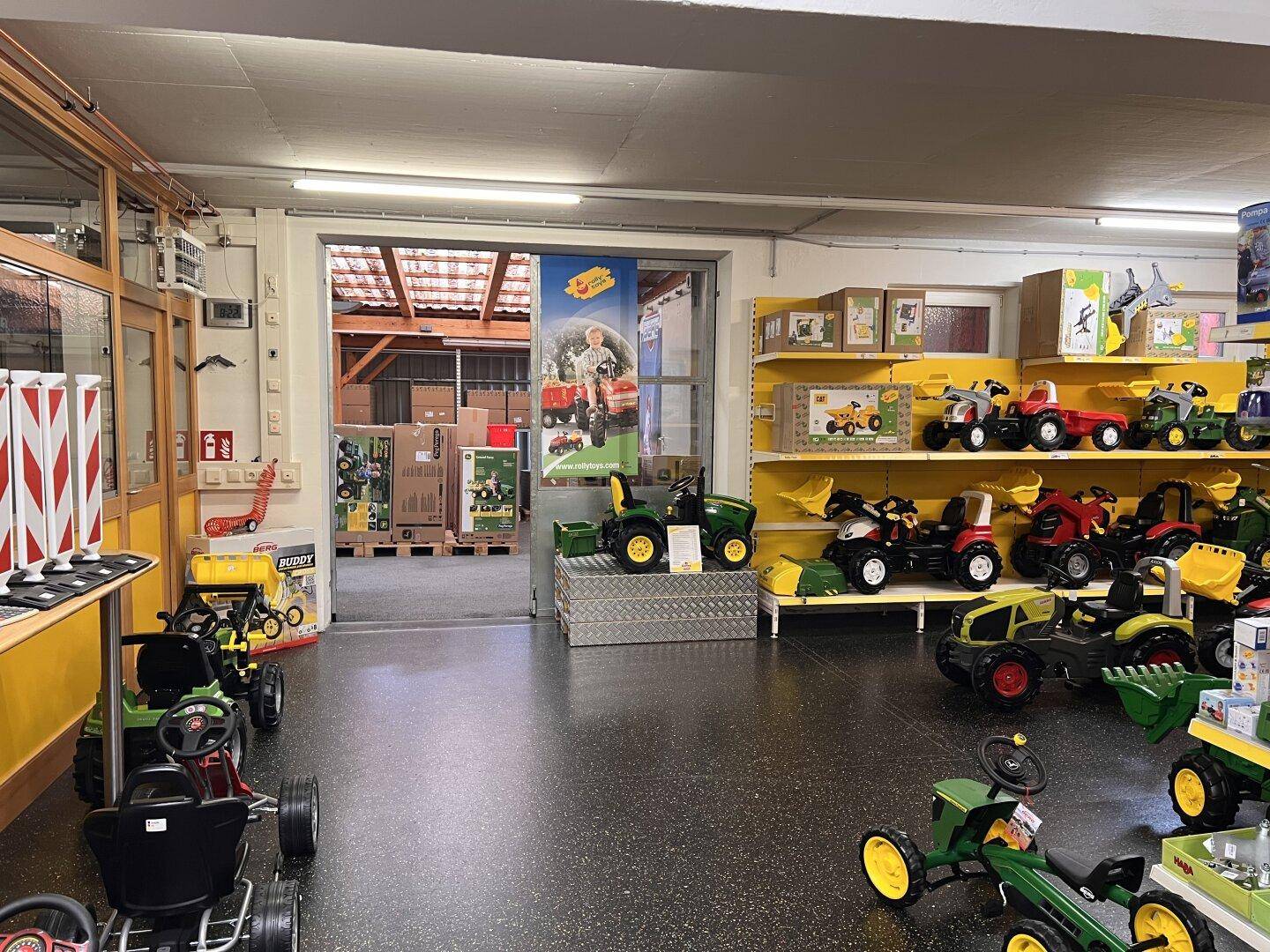 Lager- oder Ausstellungsbereich mit großen Spielzeugfahrzeugen und einem Durchgang zu einem weiteren Raum.