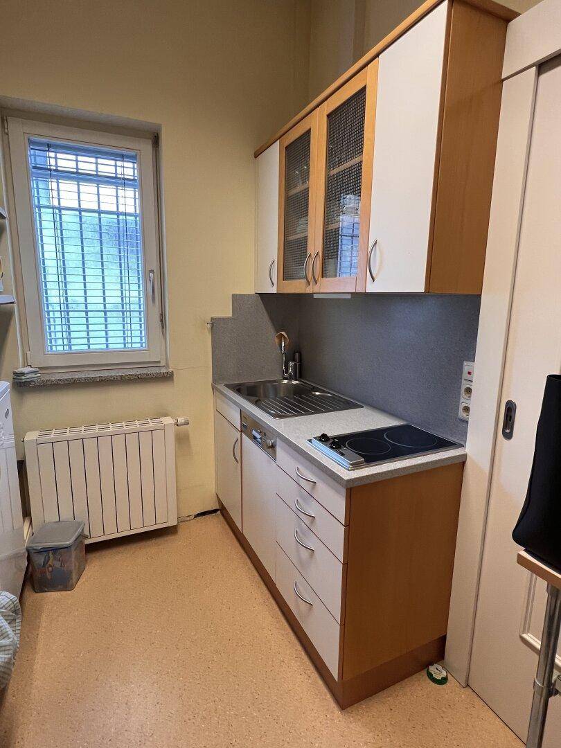 Kleine Küchenzeile mit Spüle, Kochfeld und Oberschränken, ideal für Pausenräume.