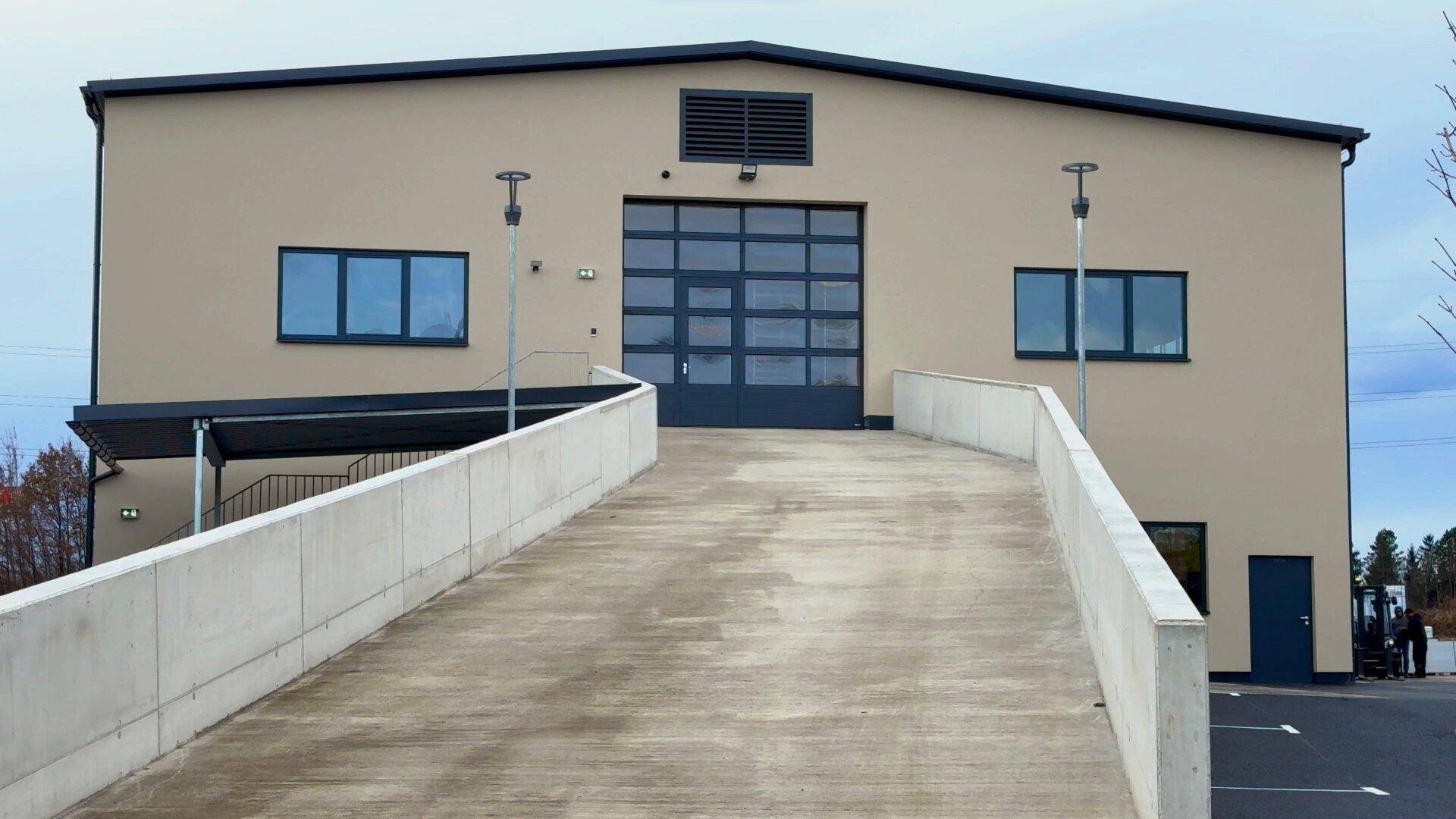 Außenansicht des Gebäudes mit einer breiten Betonrampe, großem Rolltor und beiger Fassade.