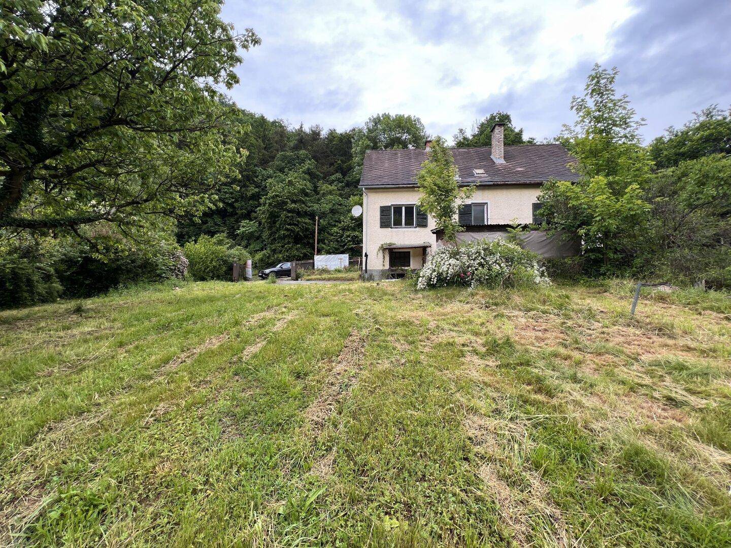 Haus mit großem Grundstück und viel Grün in ländlicher Umgebung, umgeben von Bäumen und Natur.