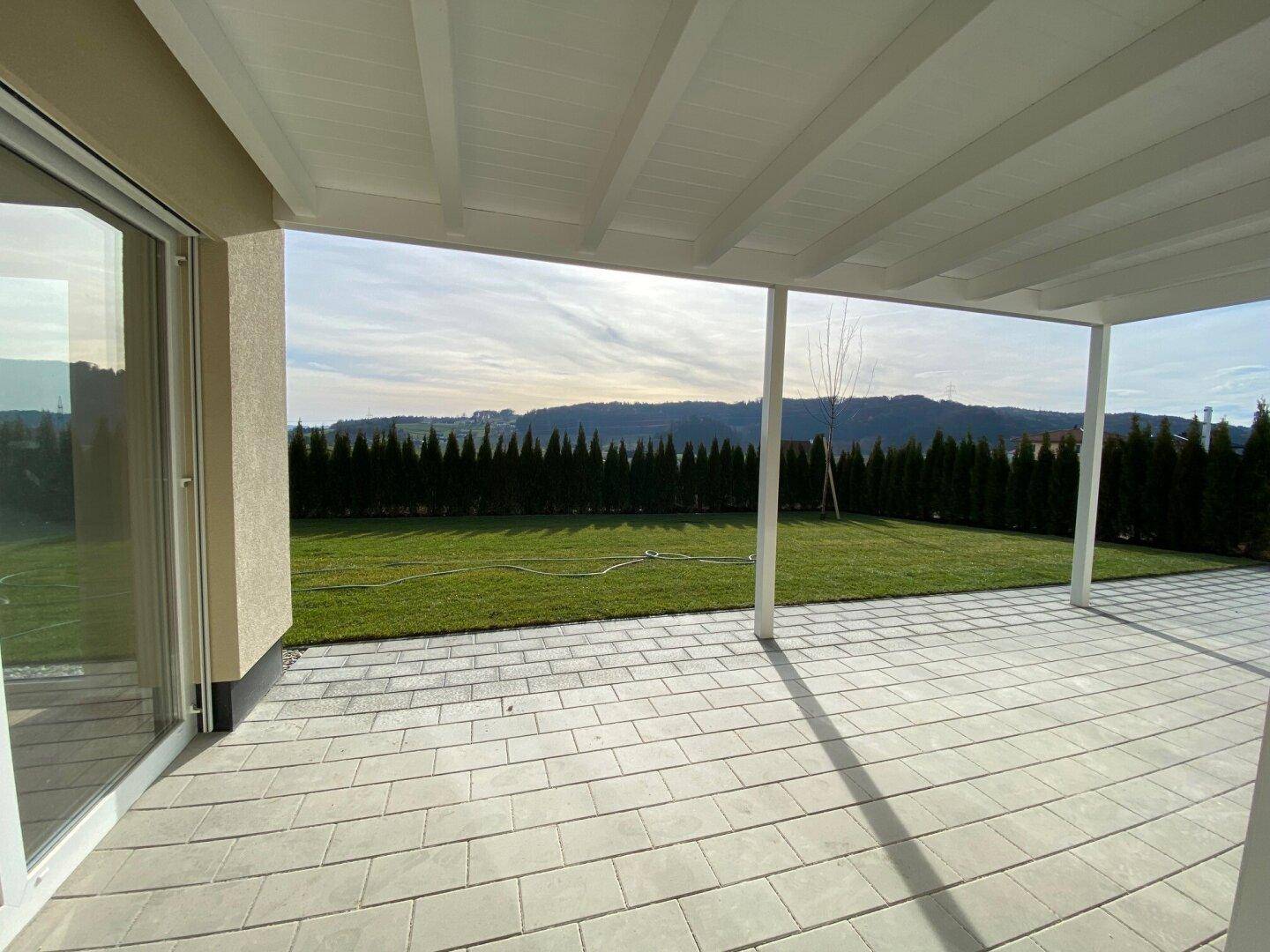 Überdachte Terrasse mit Blick auf die grüne Landschaft und den gepflegten Garten.