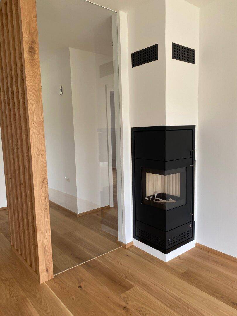 Moderner Eckkamin mit schwarzer Verkleidung und Holzelementen im Innenbereich.