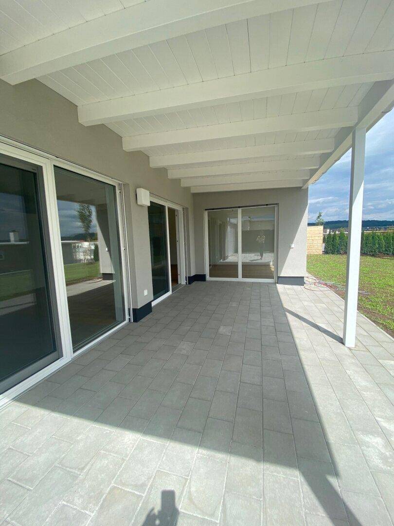Geräumige überdachte Terrasse mit Fliesenboden und Zugang zum Garten.