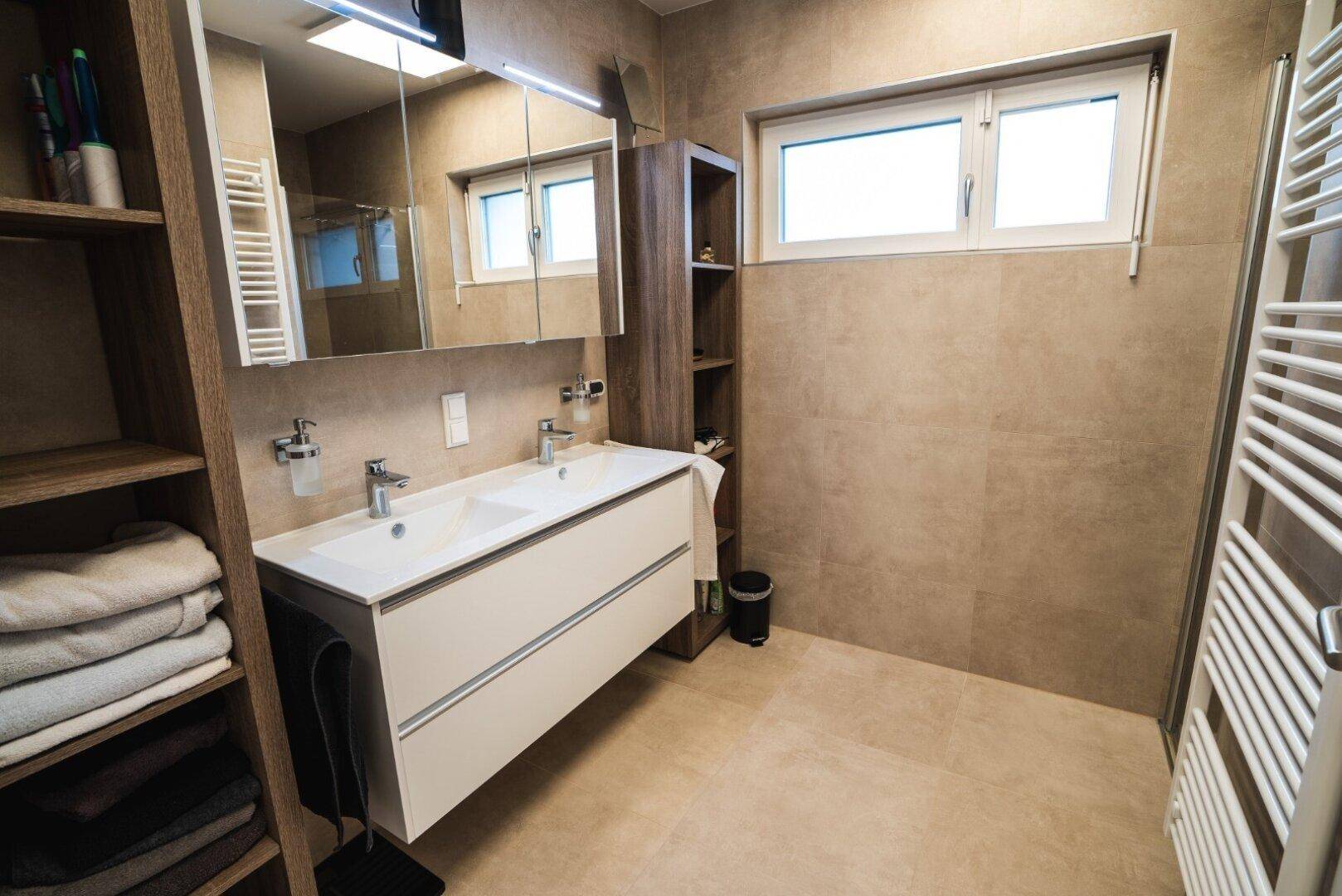 Modernes Badezimmer mit Doppelwaschbecken, großem Spiegel und beheiztem Handtuchhalter.