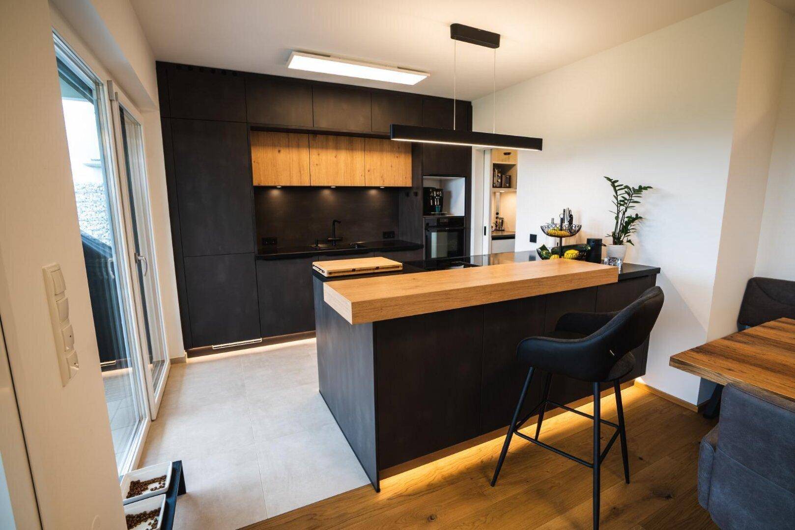 Moderne Küche mit dunklen Fronten, Holzdetails und einer Kücheninsel mit Barhockern.