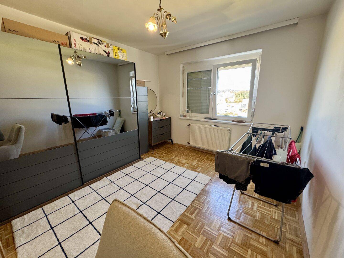Schlafzimmer mit Parkettboden, großem Kleiderschrank und Fenster mit Blick nach draußen.