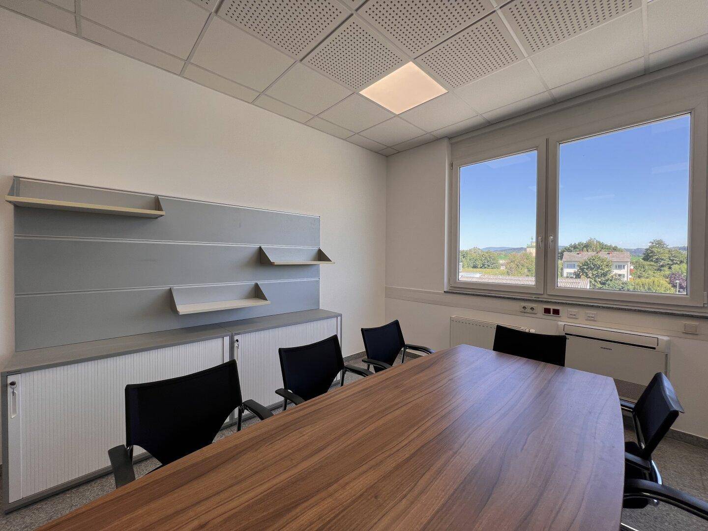 Besprechungsraum mit Holztisch, Stühlen und Fensterblick auf die Umgebung.