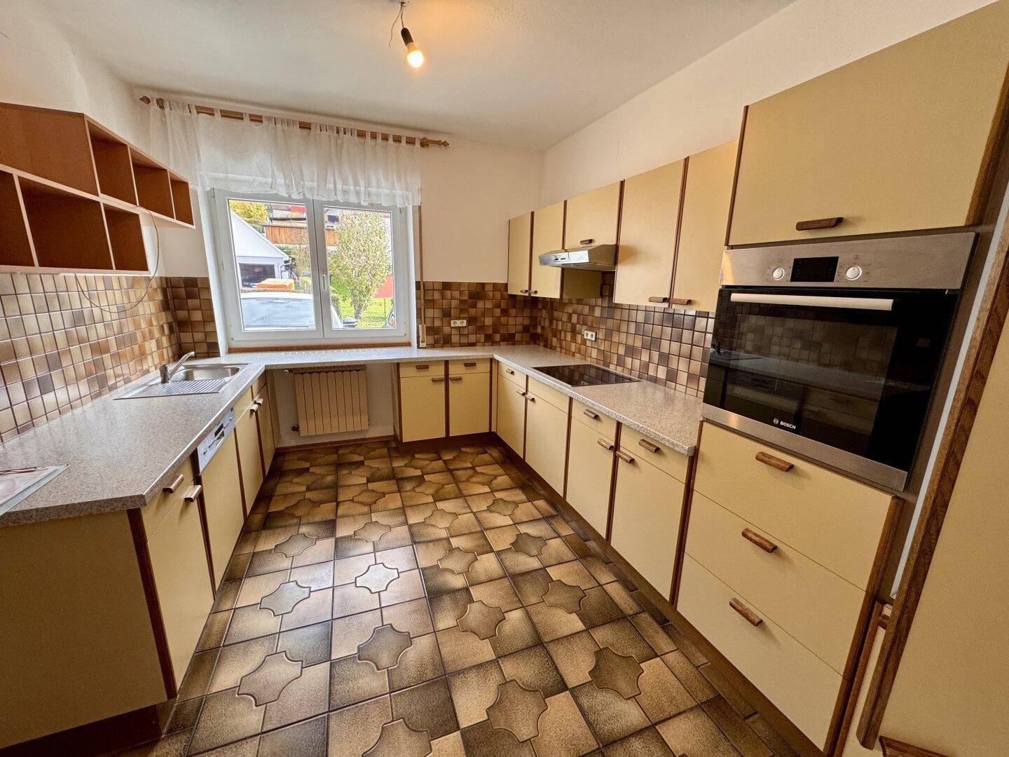 Helle Küche mit beigen Schränken, gemusterten Fliesen und integriertem Backofen.