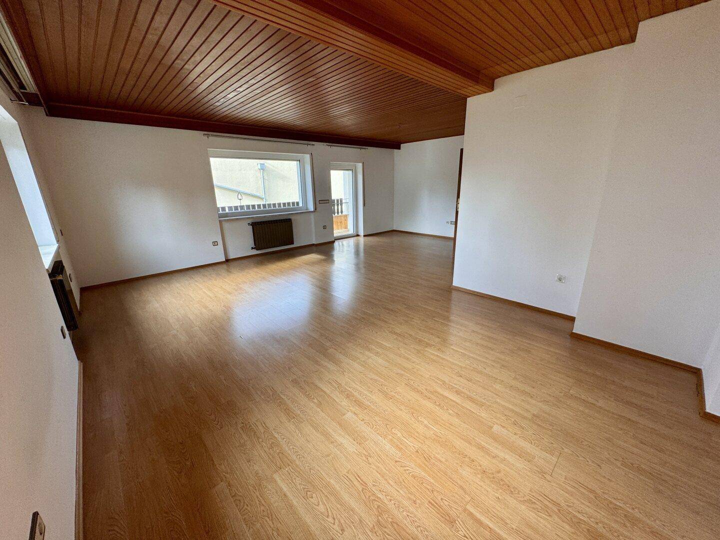 Heller Wohnbereich mit Laminatboden und Holzdecke, Zugang zu einem Balkon.