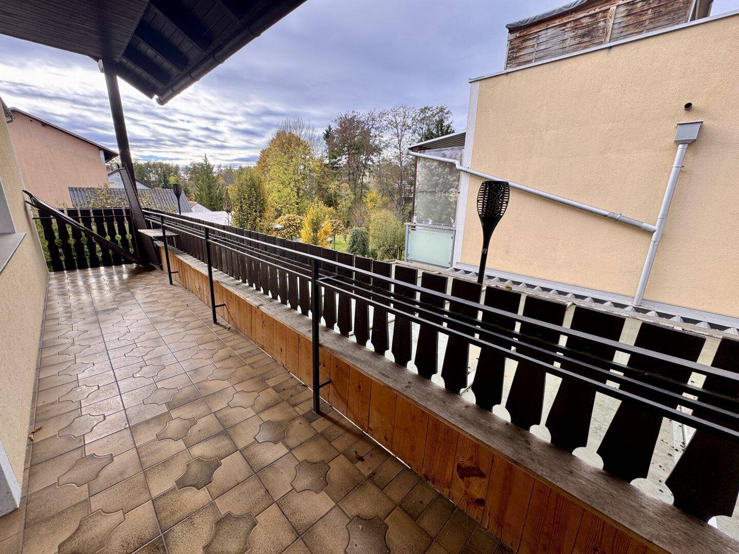 Langer Balkon mit Fliesenboden und Holzgeländer, bietet einen Blick ins Grüne.