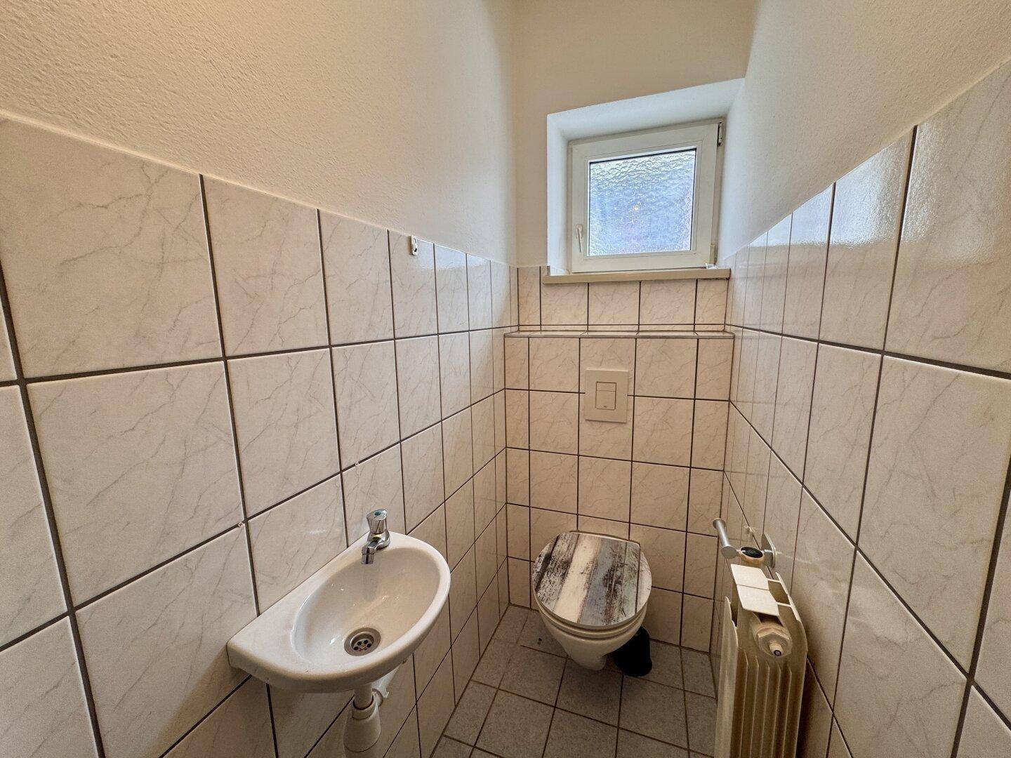 Kleines Gäste-WC mit Fenster, Wandfliesen und einem wandhängenden Waschbecken.