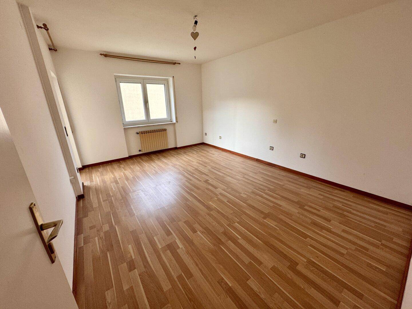 Helles Schlafzimmer mit Laminatboden und Fenster, bereit zur individuellen Gestaltung.