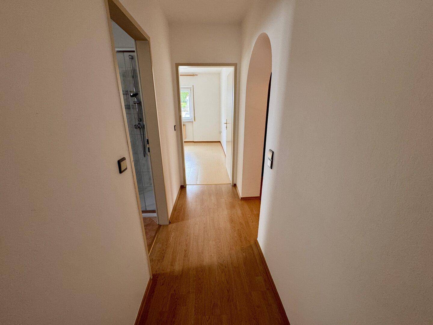 Langer Flur mit Laminatboden, der zu einem Badezimmer und weiteren Zimmern führt.