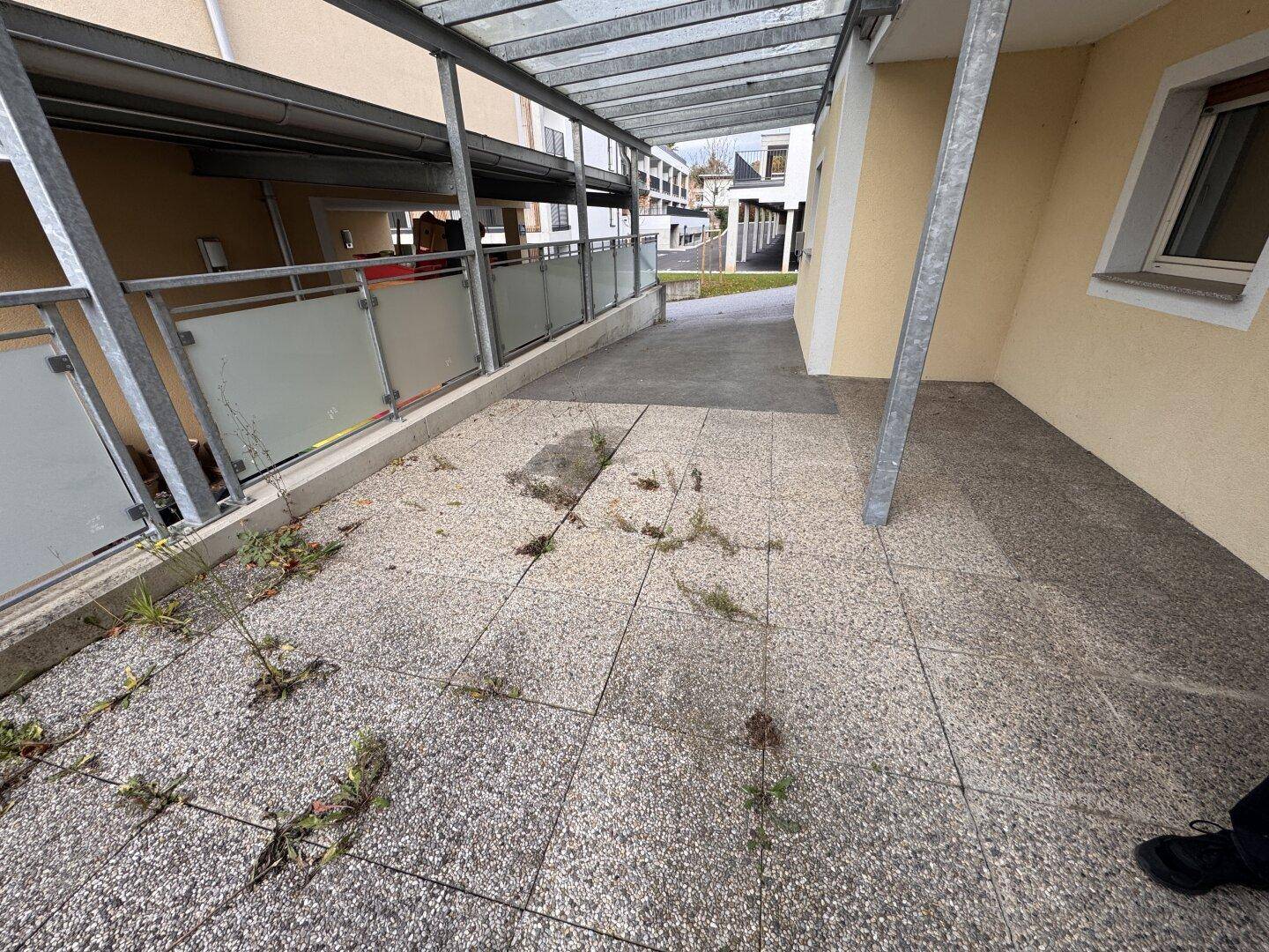 Überdachte Terrasse mit Fliesenboden und Blick auf die Umgebung, benötigt etwas Pflege.