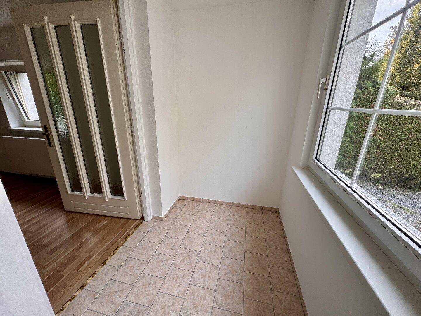 Heller Raum mit Fliesenboden und großem Fenster, ideal als kleiner Wintergarten oder Abstellraum.